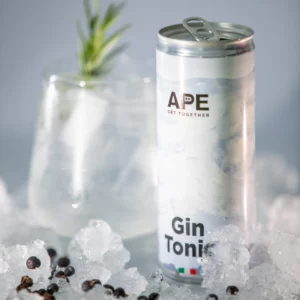 Image of a can of gin tonic in the foreground and a glass containing the cocktail in the background. The background is pastel blue, and there is crushed ice around the elements.